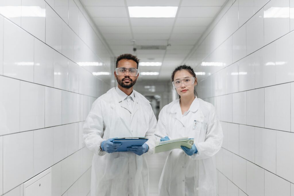 Two scientists in lab coats and goggles in a laboratory hallway conducting research.