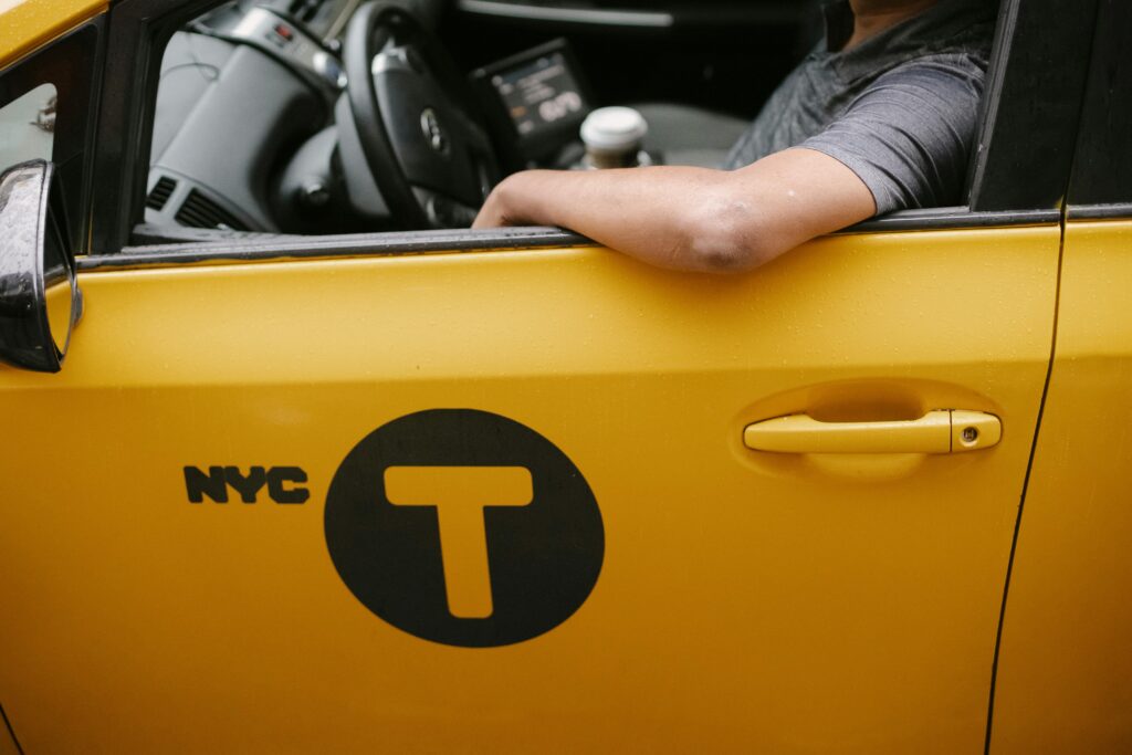 A close-up view of a yellow NYC taxi with a driver resting an arm on the window, showcasing urban transportation.